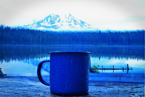 a coffee mug when camping, by lake under mountain